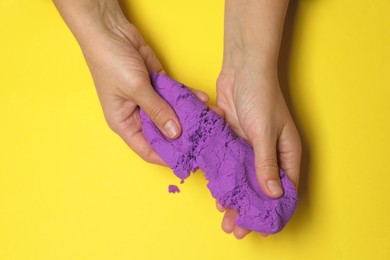 Woman playing with kinetic sand on yellow background, top view