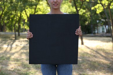Woman holding blank poster outdoors, closeup. Mockup for design	