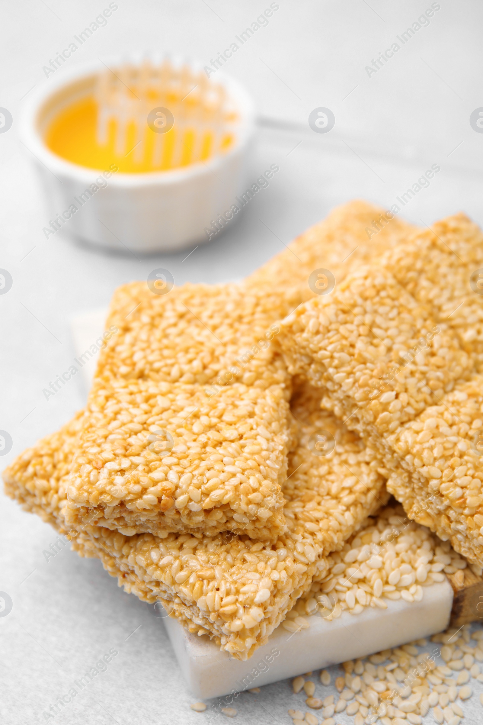 Photo of Delicious sesame kozinaki bars and honey on white table, closeup