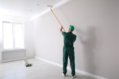 Photo of Man painting ceiling with roller in room, back view