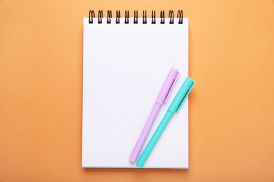 Colorful markers and notebook on orange background, top view