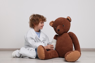 Little boy in medical uniform and toy bear with bandage indoors