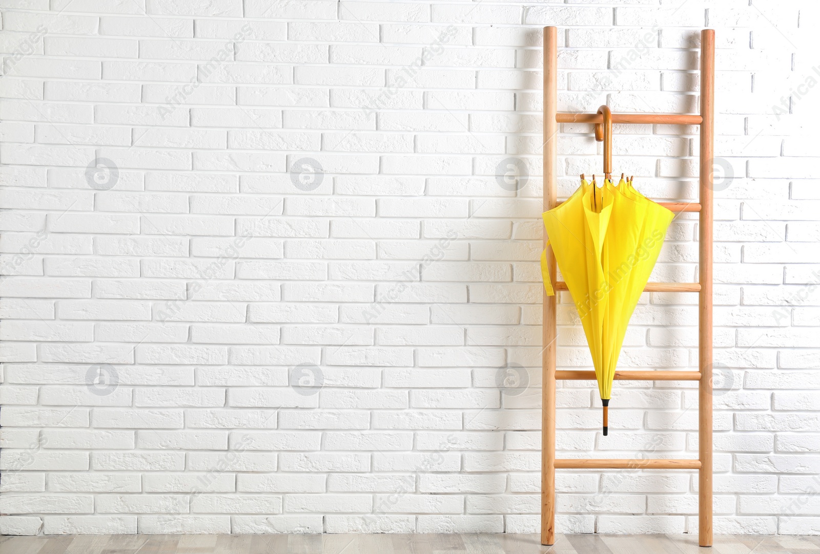 Photo of Beautiful yellow umbrella on ladder near white brick wall. Space for text
