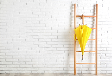 Photo of Beautiful yellow umbrella on ladder near white brick wall. Space for text