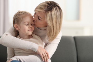 Photo of Mother kissing her daughter on sofa at home. Space for text