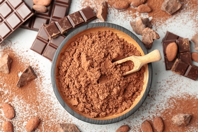 Flat lay composition with cocoa powder, beans and chocolate on light background