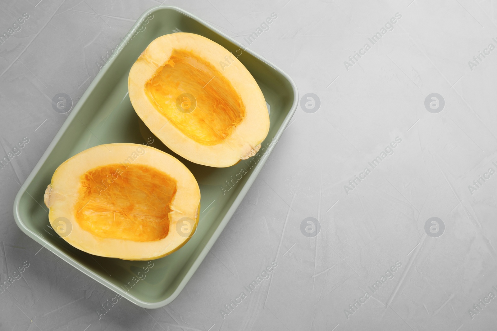 Photo of Raw spaghetti squash halves in baking dish on light table, top view. Space for text