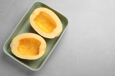 Photo of Raw spaghetti squash halves in baking dish on light table, top view. Space for text