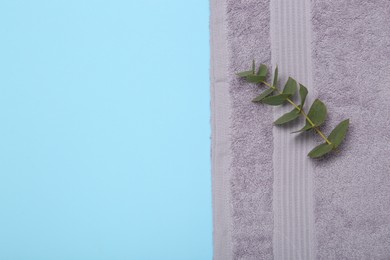 Violet terry towel and eucalyptus branch on light blue background, top view. Space for text