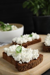 Photo of Bread with cottage cheese and basil on wooden board, closeup