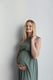 Photo of Young pregnant woman touching belly on light background