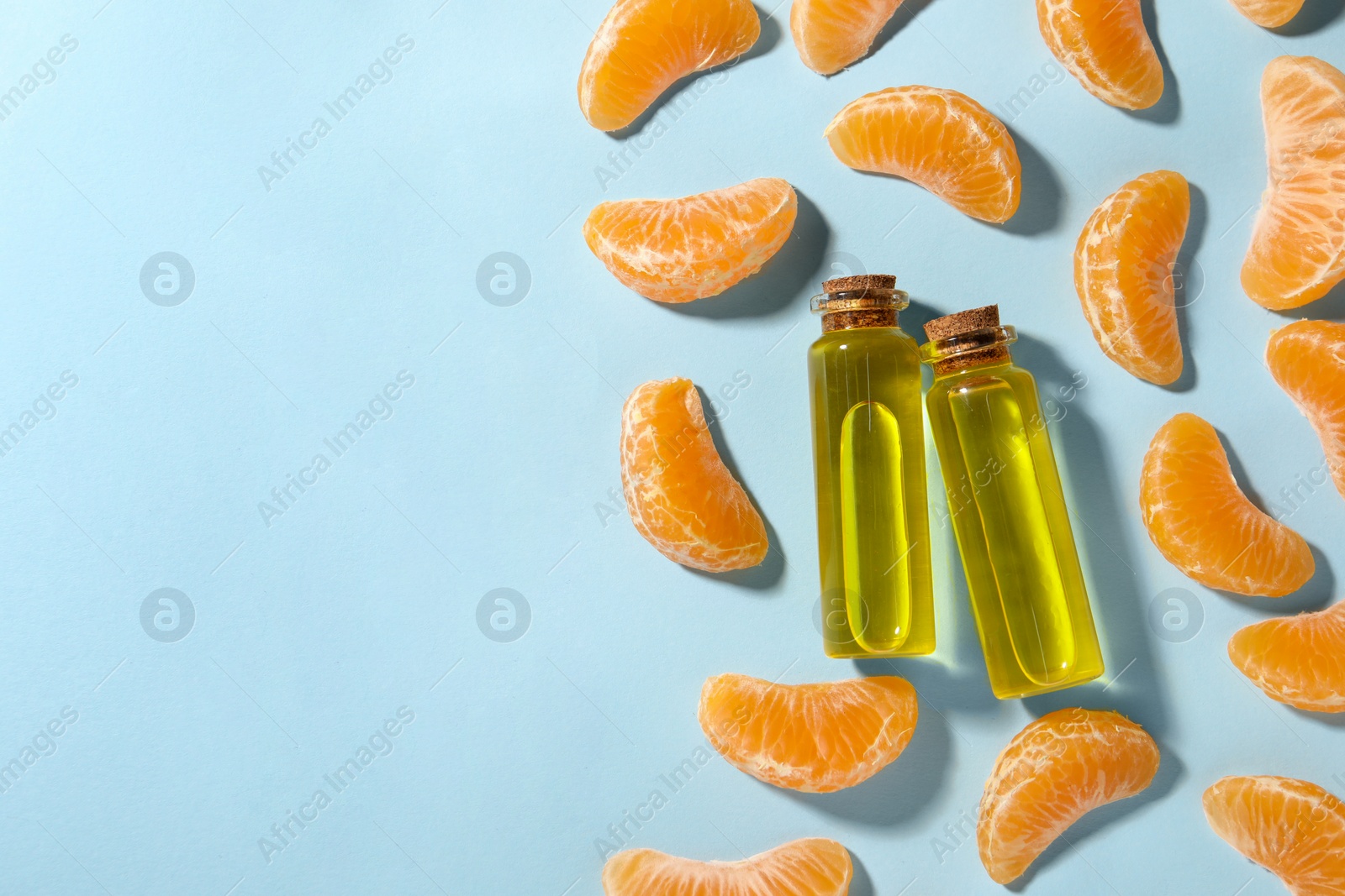 Photo of Aromatic tangerine essential oil in bottles and citrus fruits on light blue table, flat lay. Space for text