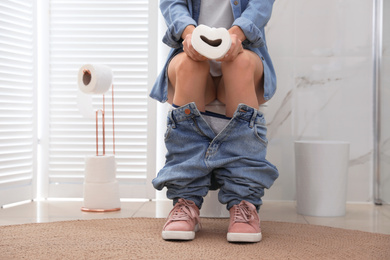 Photo of Woman with paper suffering from hemorrhoid on toilet bowl in rest room, closeup