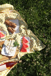 Picnic blanket with delicious food and wine on green grass outdoors, top view