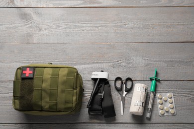 Flat lay composition with military first aid kit and tourniquet on light grey wooden table. Space for text