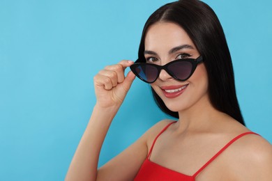 Photo of Attractive happy woman touching fashionable sunglasses against light blue background