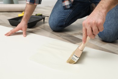 Man applying glue onto wall paper on floor, closeup