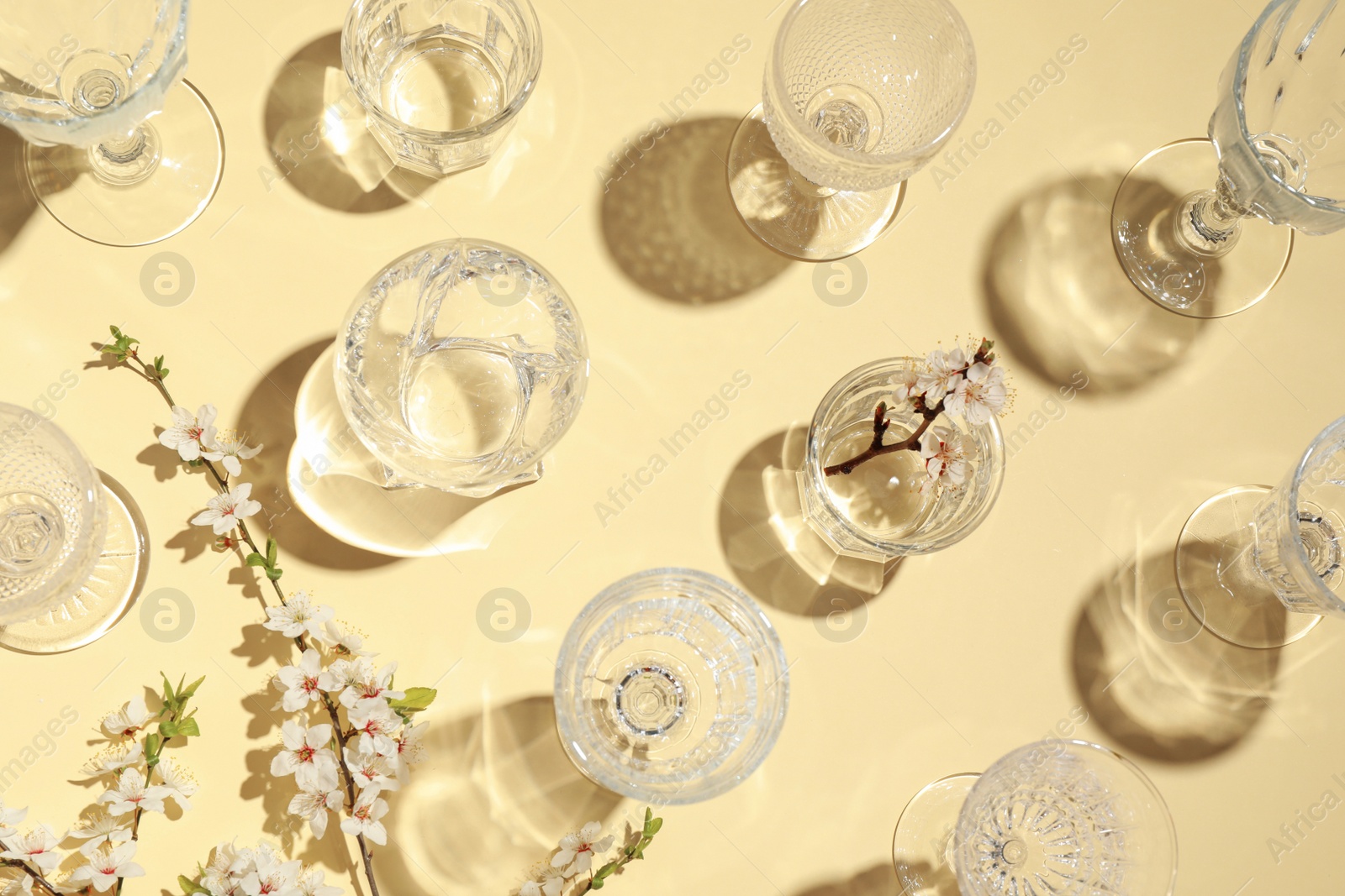 Photo of Empty glasses and twigs with flowers on beige background, flat lay