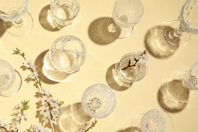 Photo of Empty glasses and twigs with flowers on beige background, flat lay