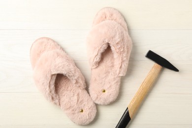 Photo of Nailed fluffy slippers and hammer on white wooden floor, flat lay. Celebrating April Fool's day
