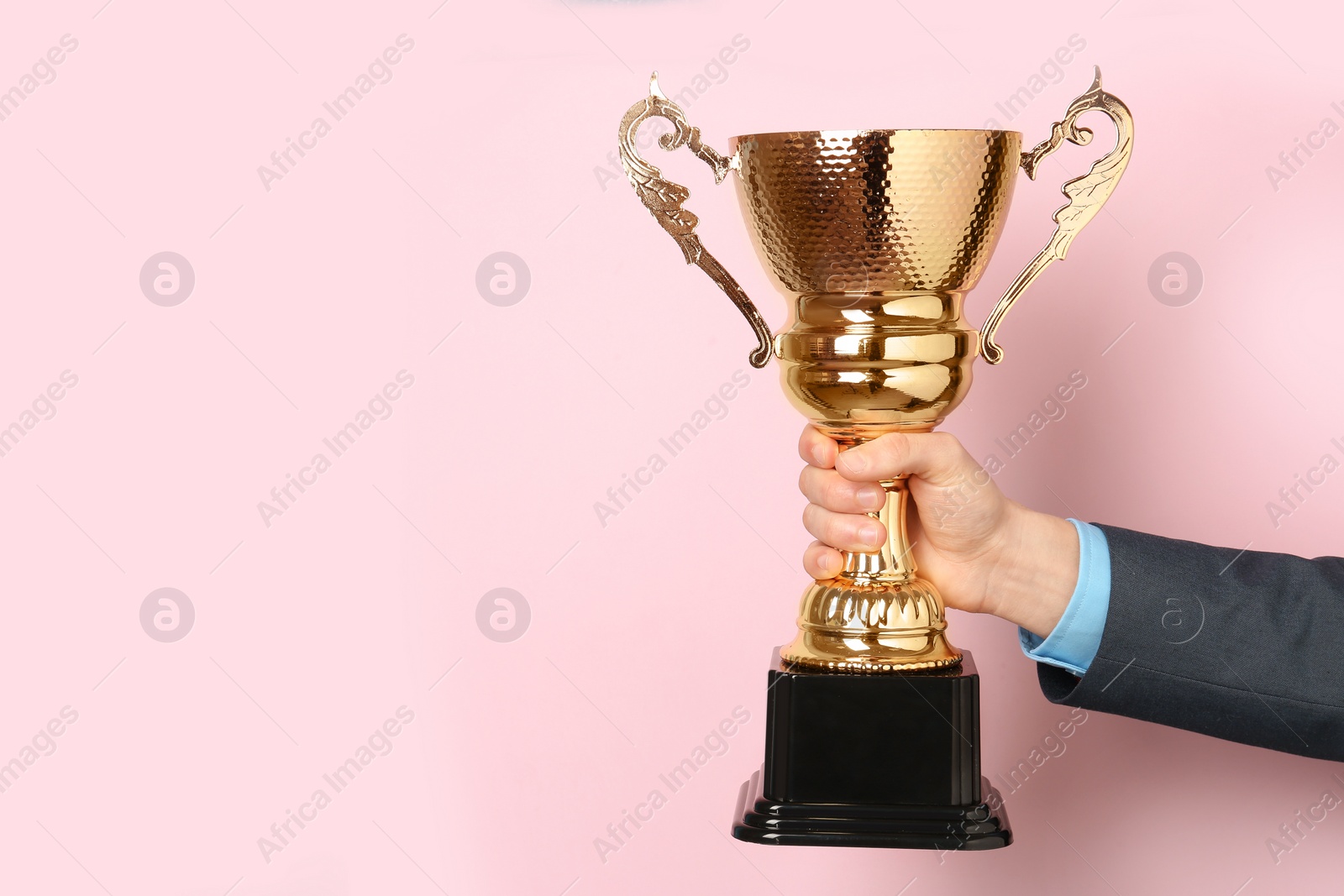 Photo of Man holding golden trophy cup on color background, closeup. Space for text