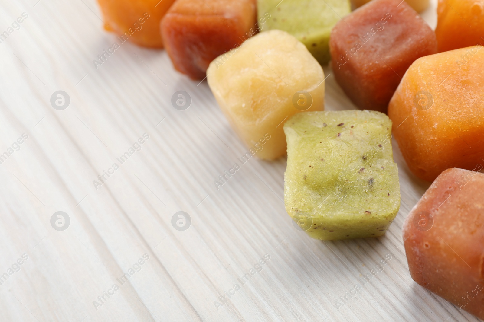 Photo of Different frozen fruit puree cubes on white wooden table, closeup. Space for text