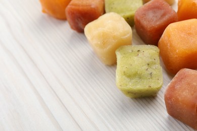 Different frozen fruit puree cubes on white wooden table, closeup. Space for text