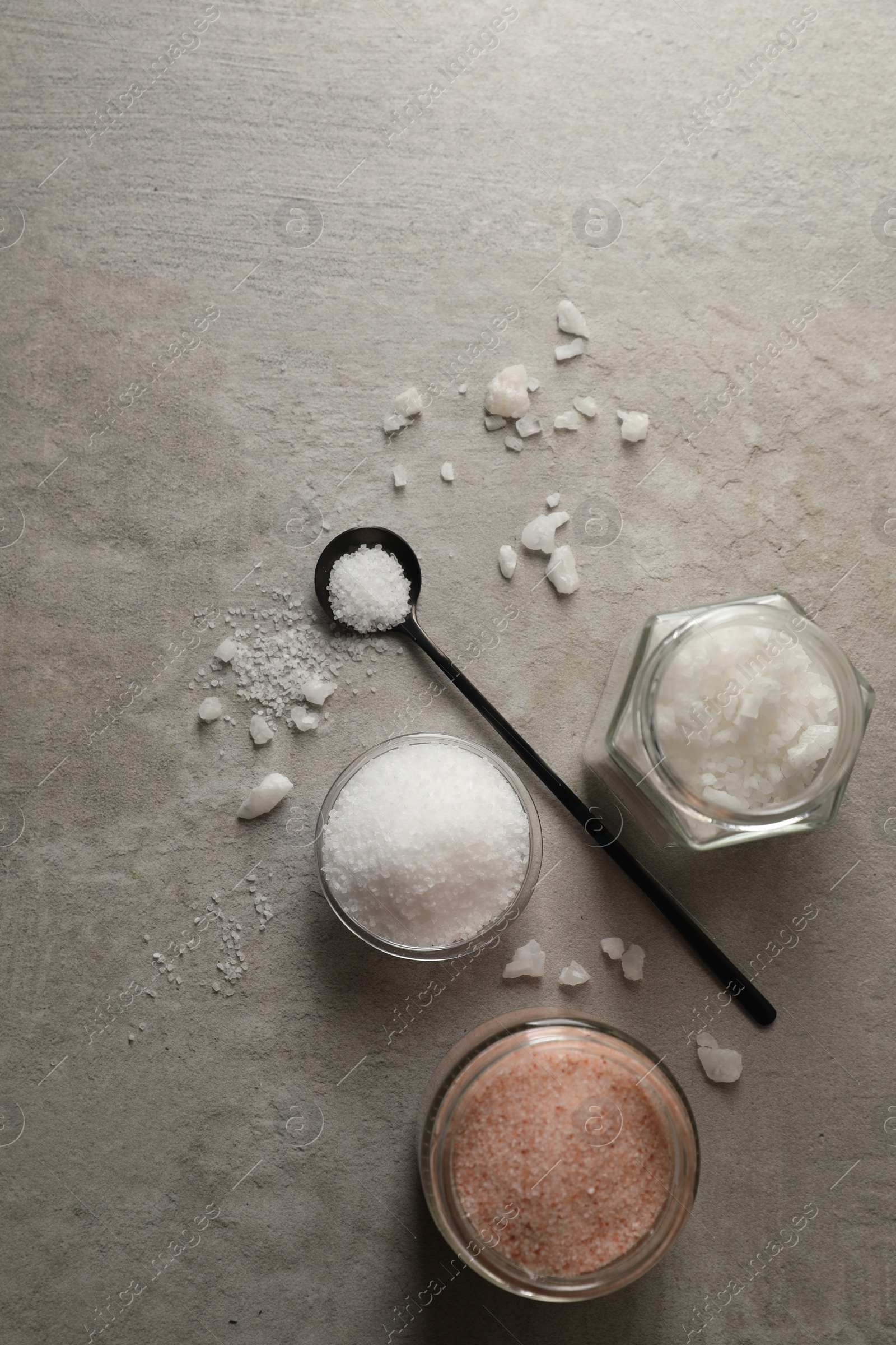 Photo of Different natural salt on grey textured table, flat lay