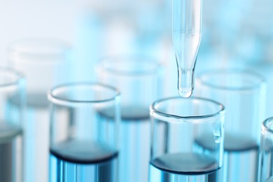 Photo of Dripping liquid from pipette into test tube on light background, closeup