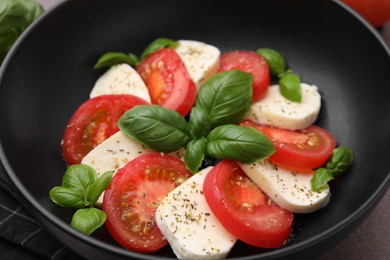 Photo of Caprese salad with tomatoes, mozzarella, basil and spices in bowl, closeup