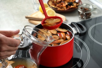 Woman pouring compot into glass pitcher near stove, closeup