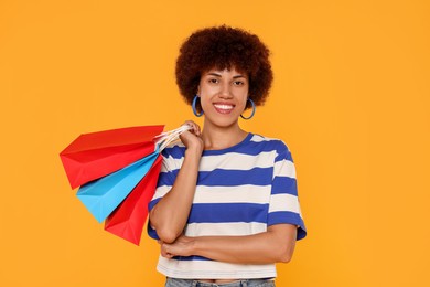 Happy young woman with shopping bags on orange background