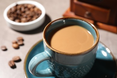 Delicious coffee with milk in cup and beans on light table, closeup