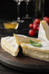 Tasty brie cheese with basil on wooden board, closeup