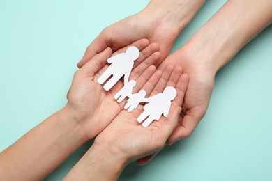 Couple holding paper family cutout on turquoise background, top view