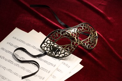 Elegant face mask and music sheets on red fabric. Theatrical performance