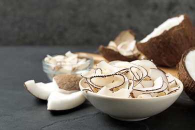 Photo of Tasty coconut chips in bowl on black table. Space for text