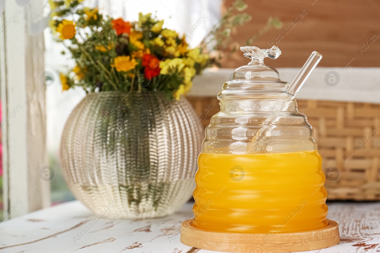 Photo of Delicious fresh honey and beautiful flowers on white wooden table indoors, space for text