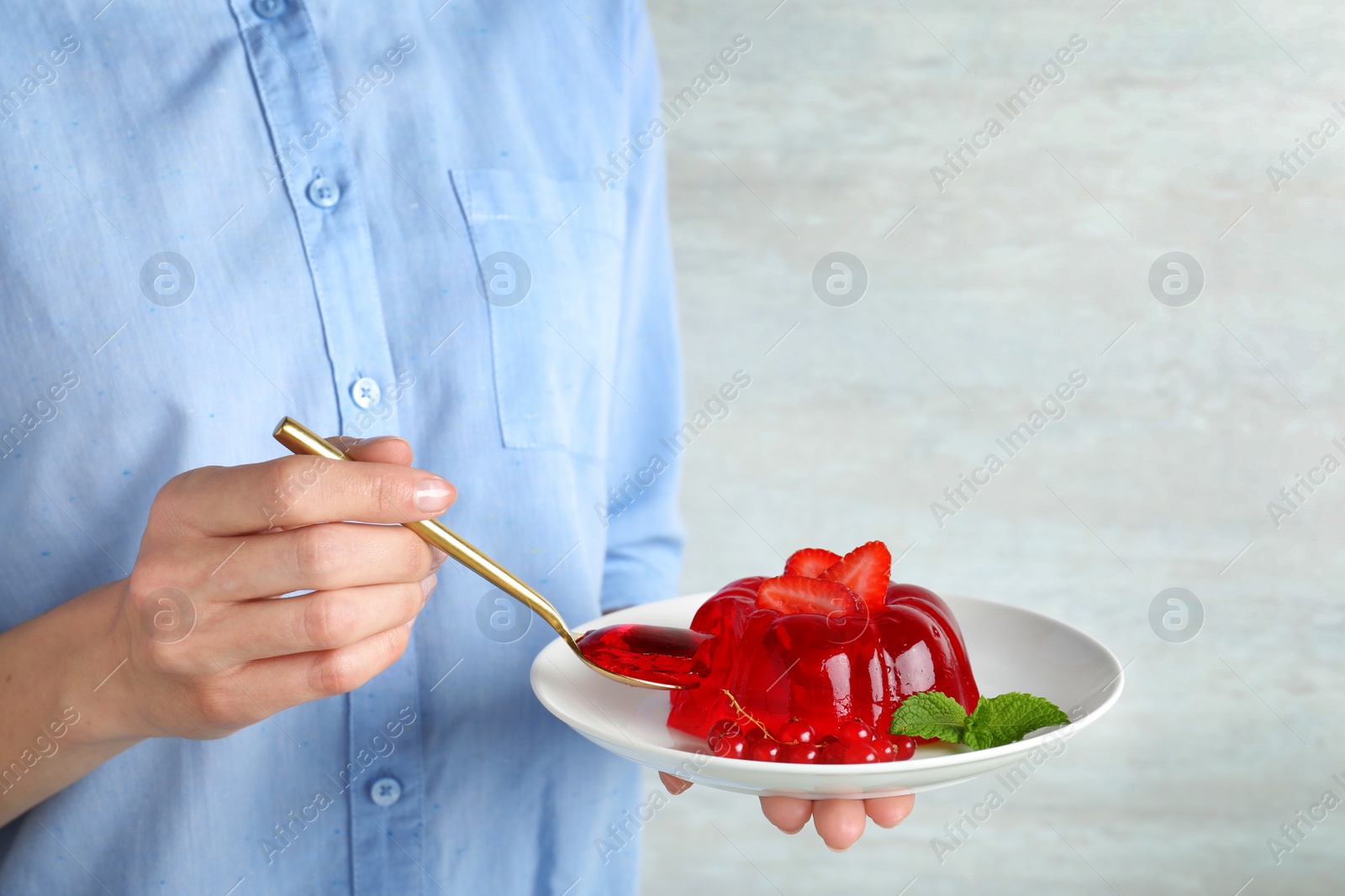 Photo of Woman eating delicious fresh red jelly against light background, closeup