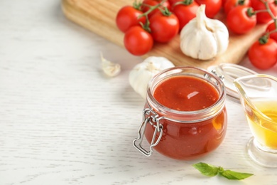 Jar of tomato sauce and vegetables on white wooden table, space for text