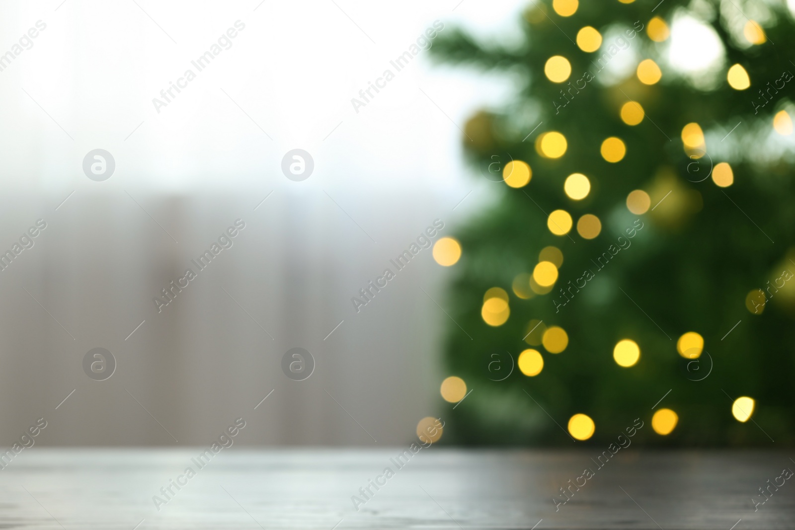 Photo of Blurred view of fir tree with glowing Christmas lights near table indoors