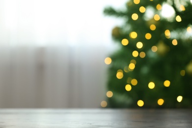 Photo of Blurred view of fir tree with glowing Christmas lights near table indoors