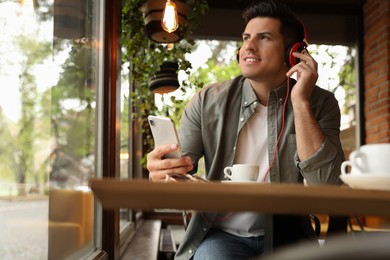 Handsome man with headphones and smartphone listening to music in cafe