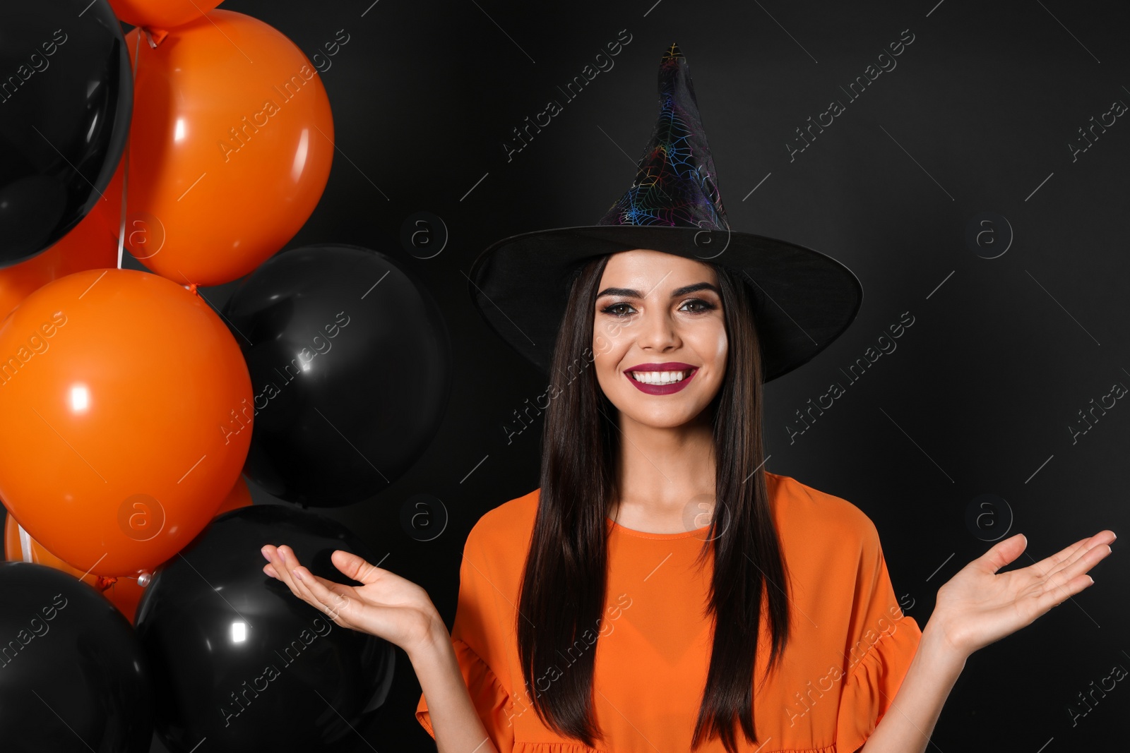 Photo of Beautiful woman wearing witch costume with balloons for Halloween party on black background