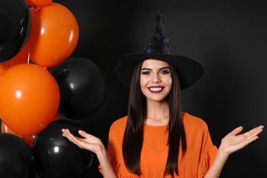 Beautiful woman wearing witch costume with balloons for Halloween party on black background