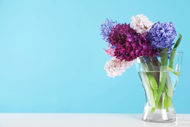 Photo of Beautiful hyacinths in glass vase on table against color background, space for text. Spring flowers