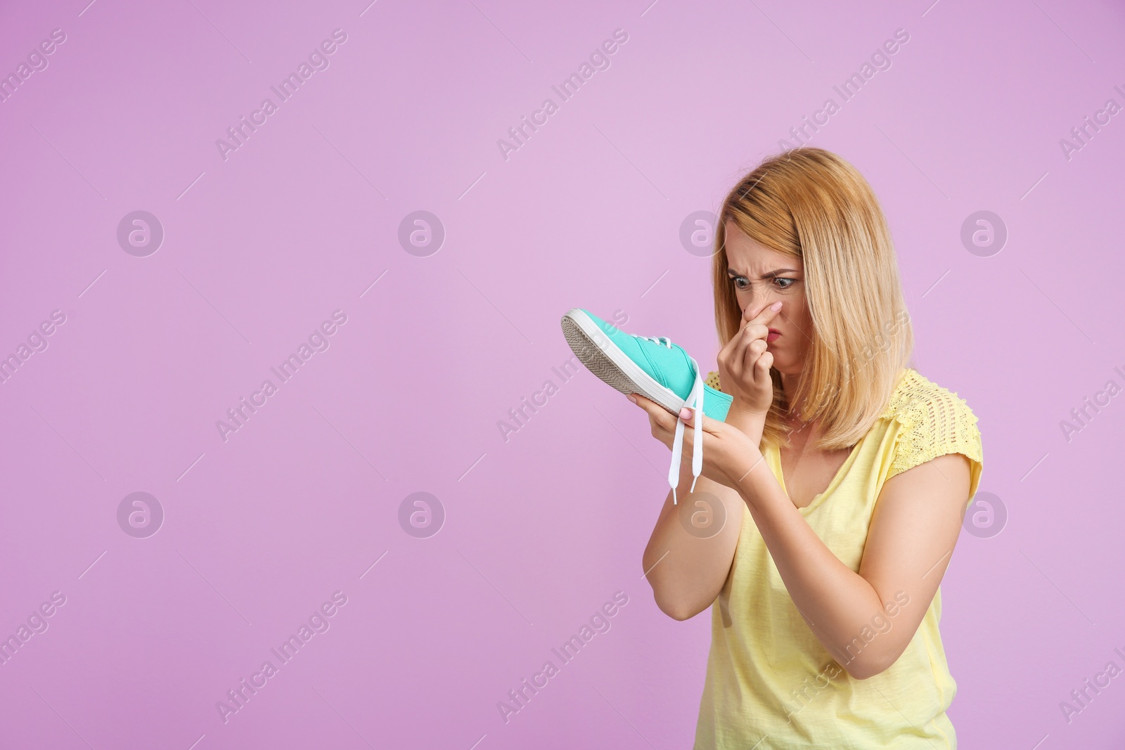 Photo of Young woman with stinky shoe on color background. Air freshener