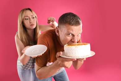 Greedy man hiding tasty cake from woman on pink background