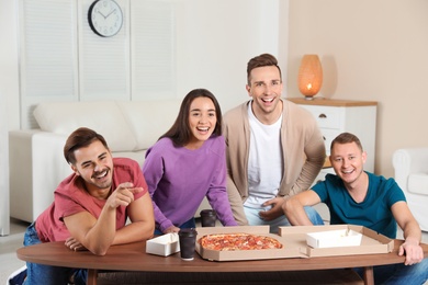 Photo of Group of friends with tasty food laughing while watching TV at home