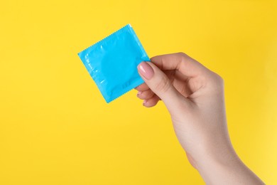 Woman holding condom on yellow background, closeup